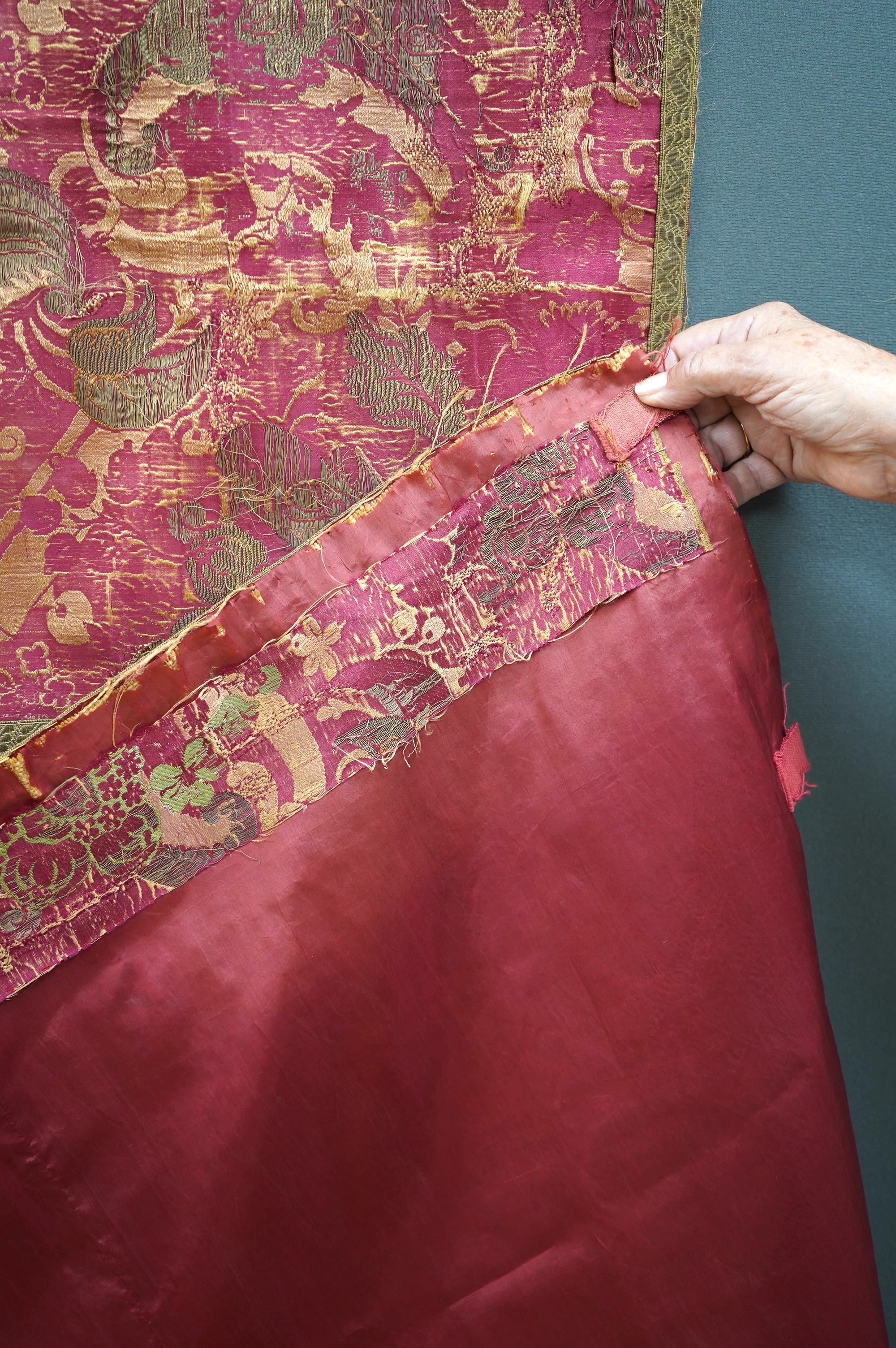 A fine 17th century Italian crimson silk brocade wall hanging, originally woven with gold threads and polychrome silks in a large ornate floral pattern, possibly part of a larger hanging, the front now edged with later n